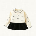 Cream knit top with bow embroidery and pleated black skirt, front view